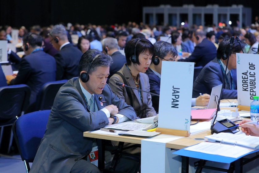 Photo of the "conversation" on trade and sustainable development, showing a large, packed room with hundreds of delegates seated along rows of tables. In the foreground, a Japanese delegate speaking